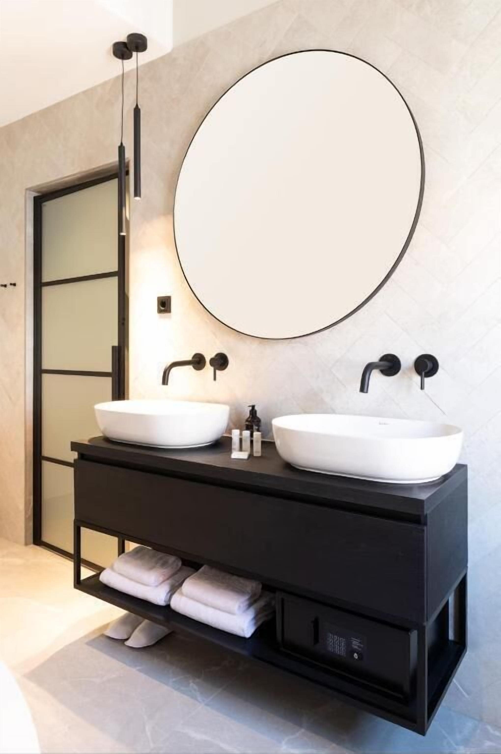 A modern bathroom with two white vessel sinks, a large round mirror, and a black vanity with built-in storage.