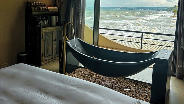 Une chambre avec un grand lit, une armoire en bois, une machine à café et une vue sur la mer par la fenêtre.