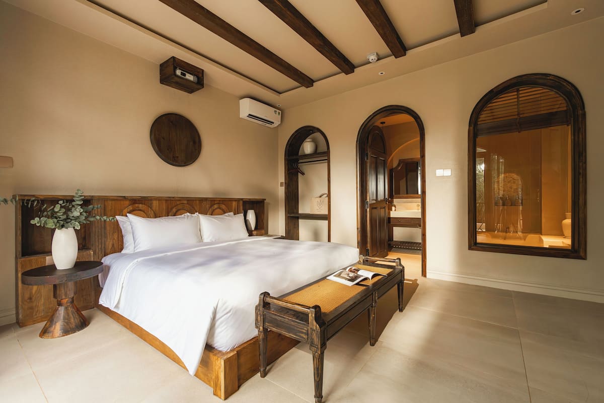 Une chambre à coucher avec un lit en bois, une table de chevet ornée d’un vase et une grande fenêtre.