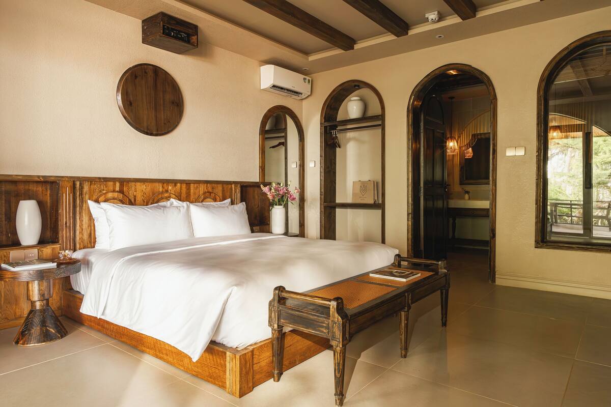 Une chambre spacieuse avec un grand lit, une tête de lit en bois et une petite table en bois.