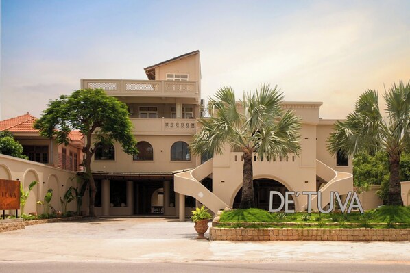 Un hôtel moderne doté d’une cour intérieure, de palmiers et d’une enseigne indiquant « DE’TUVA ».