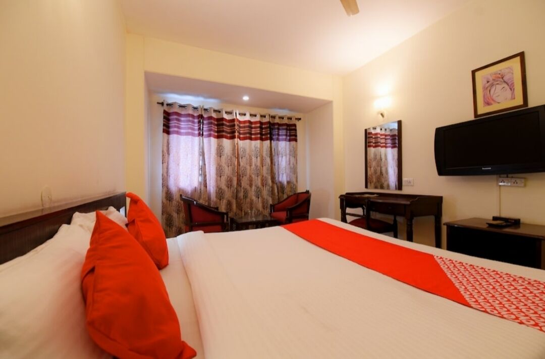 Una habitación de hotel con cama, escritorio, silla, televisión y ventana con cortinas.