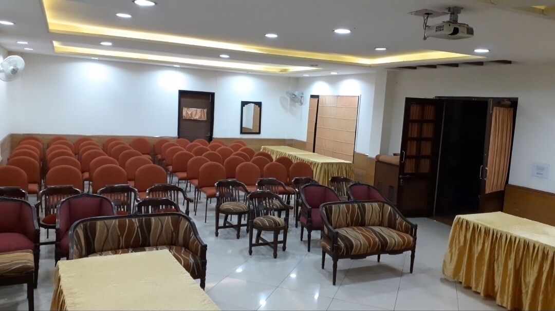 Un salón de conferencias con filas de sillas, mesas y un proyector.