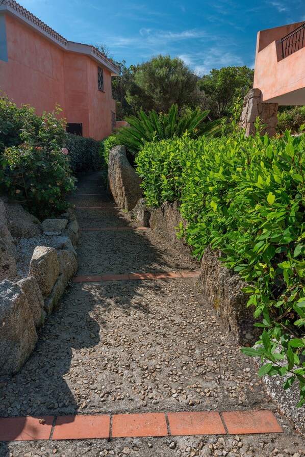 Un sendero que lleva a un edificio con techo de tejas y una pared de piedra a un lado.
