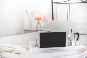 Ein Bett mit einem weißen Tablett, das eine Kaffeemaschine und eine Tasse hält, eine Nachttischlampe und eine Wand mit einem dekorativen Gegenstand.