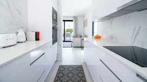 A modern kitchen with white cabinetry, a black stove, and a view to a living area. - 125 Quinta do Paraiso, elegant Holiday Villa! (Carvoeiro)