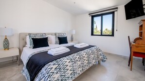 A bedroom with a bed, two bedside tables with lamps, a TV mounted on the wall, and a window with a view. - 125 Quinta do Paraiso, elegant Holiday Villa! (Carvoeiro)