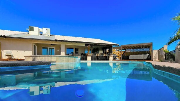 A swimming pool with a clear blue water surface, a covered patio area with outdoor furniture, and a house with a tiled roof and windows. - Luxury Retreat Pool House with spectacular views!

 (Lake Havasu City)