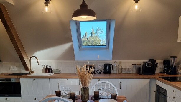 A cozy kitchen with a dining table, two white chairs, a hanging light fixture, and a view through a skylight.
