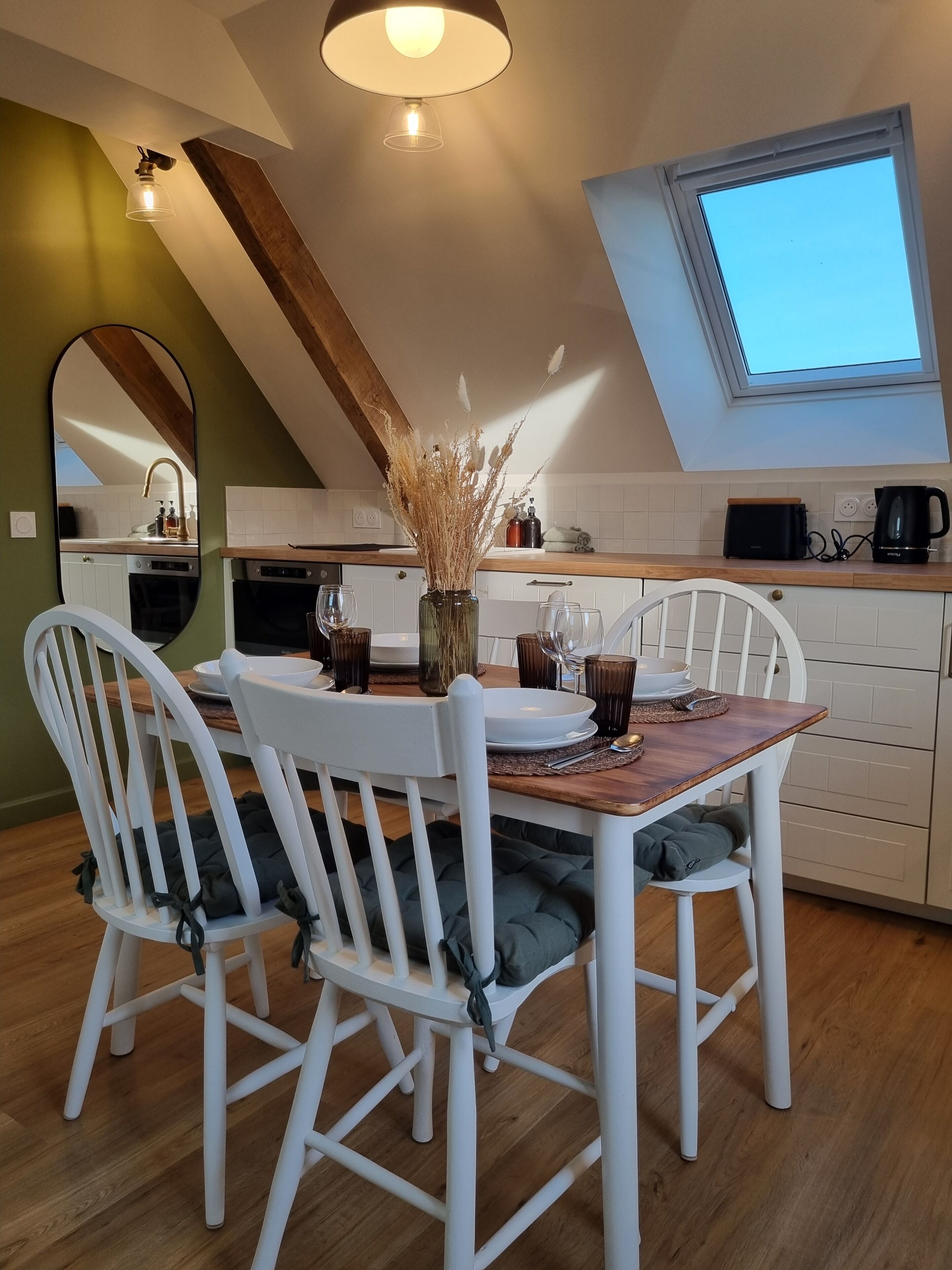 Et moderne køkken med spisebord, hvide stole og et ovenlysvindue.