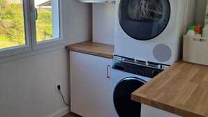 A laundry room with a front-loading washer and dryer, a window with a view of greenery, and a white wall.