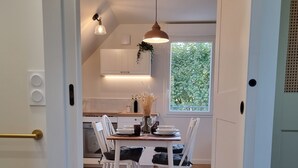 A modern kitchen with white cabinets, a dining area with a wooden table and white chairs, and a large window providing natural light.