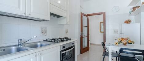 Een koelkast, een oven, een kookplaat, kookgerei, borden en bestek