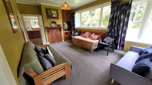 A cozy living room with a sofa, a bed, and a dining area. - Huāki Punakaiki Bach (Punakaiki)