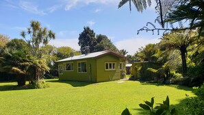 A green house with a fenced yard, surrounded by various trees and shrubs. - Huāki Punakaiki Bach (Punakaiki)