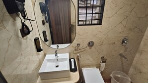 A bathroom with a white sink, mirror, and toilet. There is a hairdryer on the wall and a small window with bars. - Light House Suites Hubballi (Hubli)
