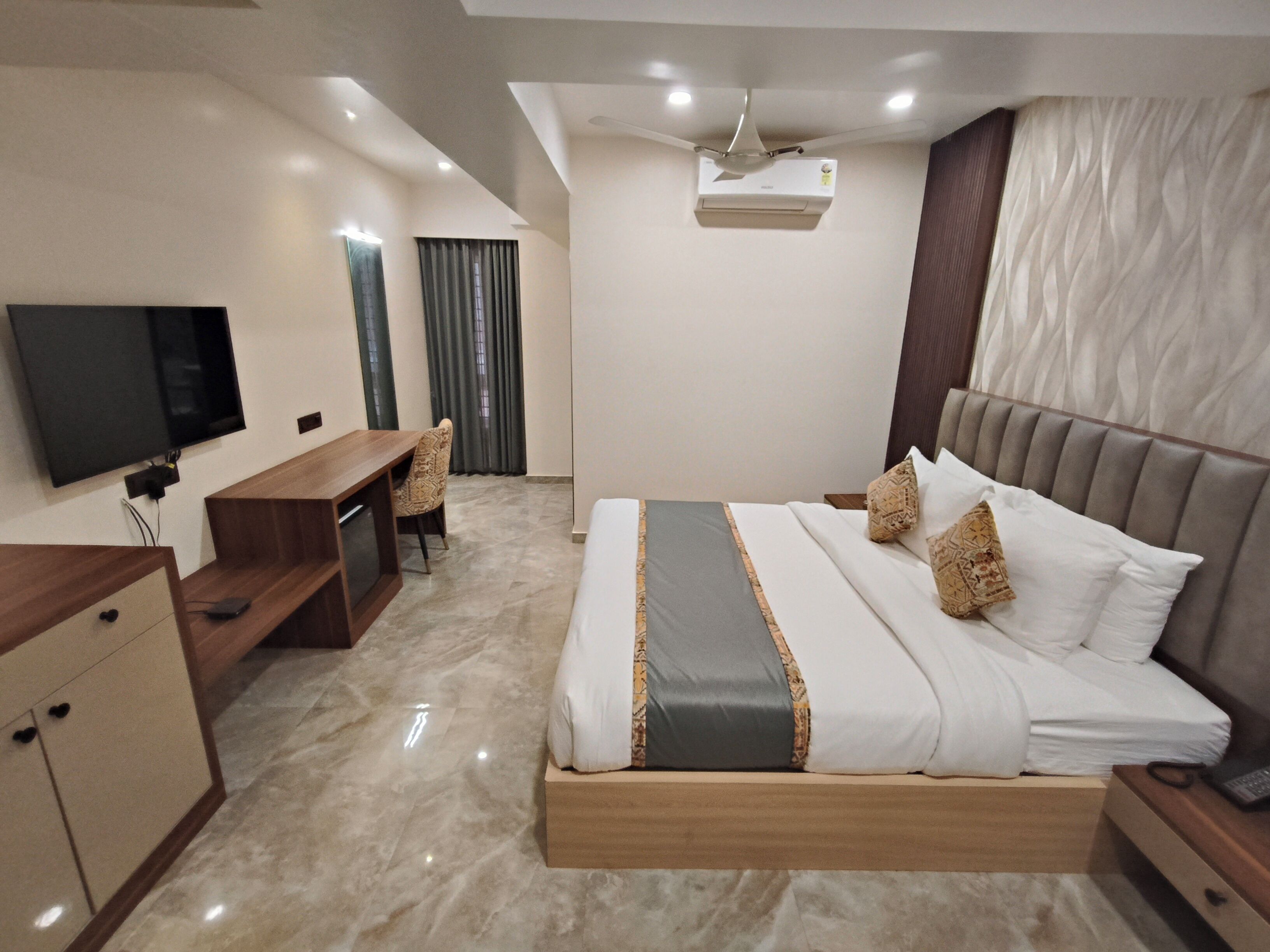 Une chambre d’hôtel moderne équipée d’un lit, d’un bureau, d’une chaise, d’une télévision et d’un ventilateur de plafond.