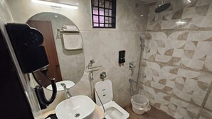 A modern bathroom with a round mirror, a white sink, a toilet, and a shower. - Light House Suites Hubballi (Hubli)