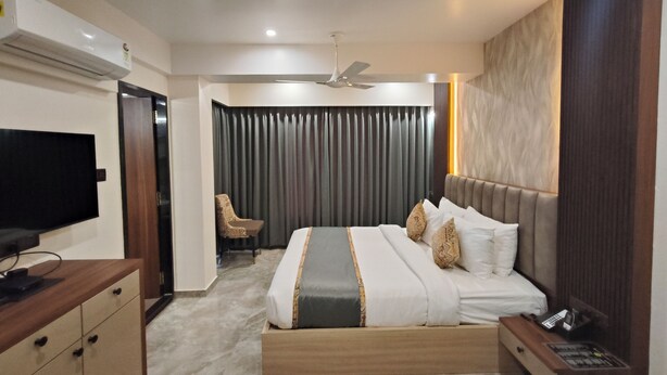 A modern hotel room with a bed, a desk, a chair, a television, and a ceiling fan. - Light House Suites Hubballi (Hubli)
