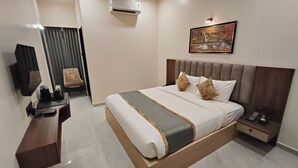 A modern hotel room with a large bed, a desk, a chair, a TV, and an air conditioning unit. - Light House Suites Hubballi (Hubli)