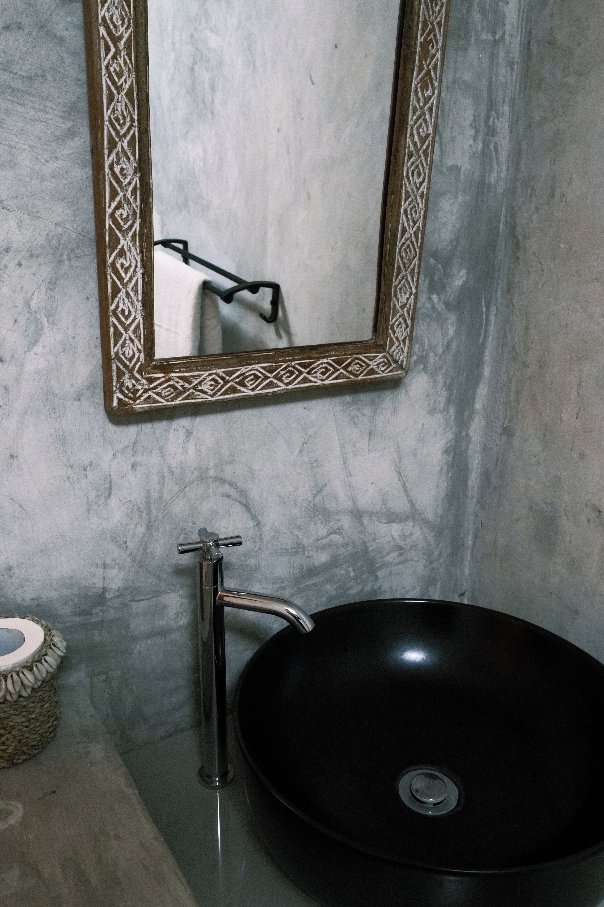 A bathroom with a black sink, a mirror with a decorative frame, and a towel holder.