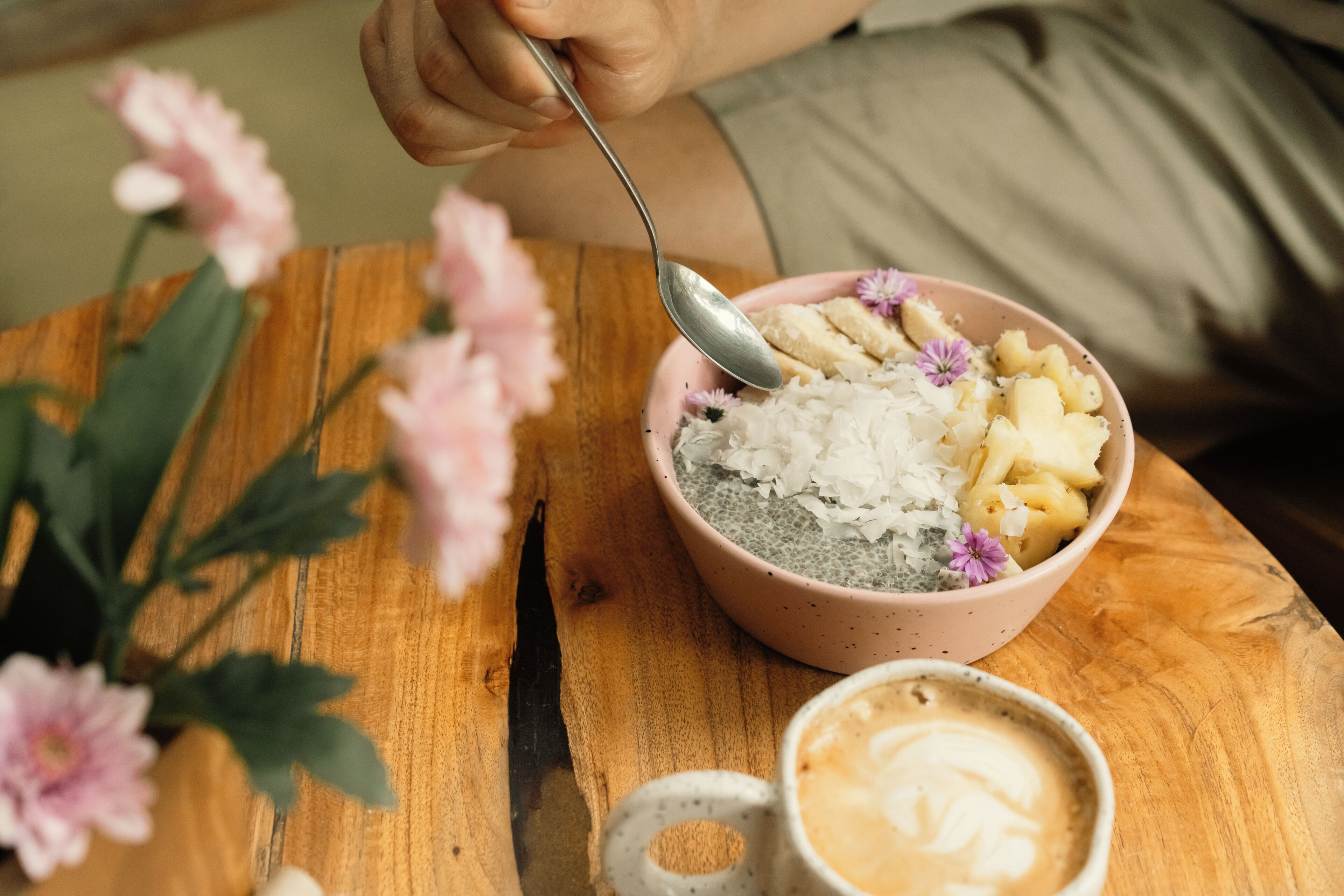 Un bol de nourriture avec une cuillère, une tasse de café et une table en bois.