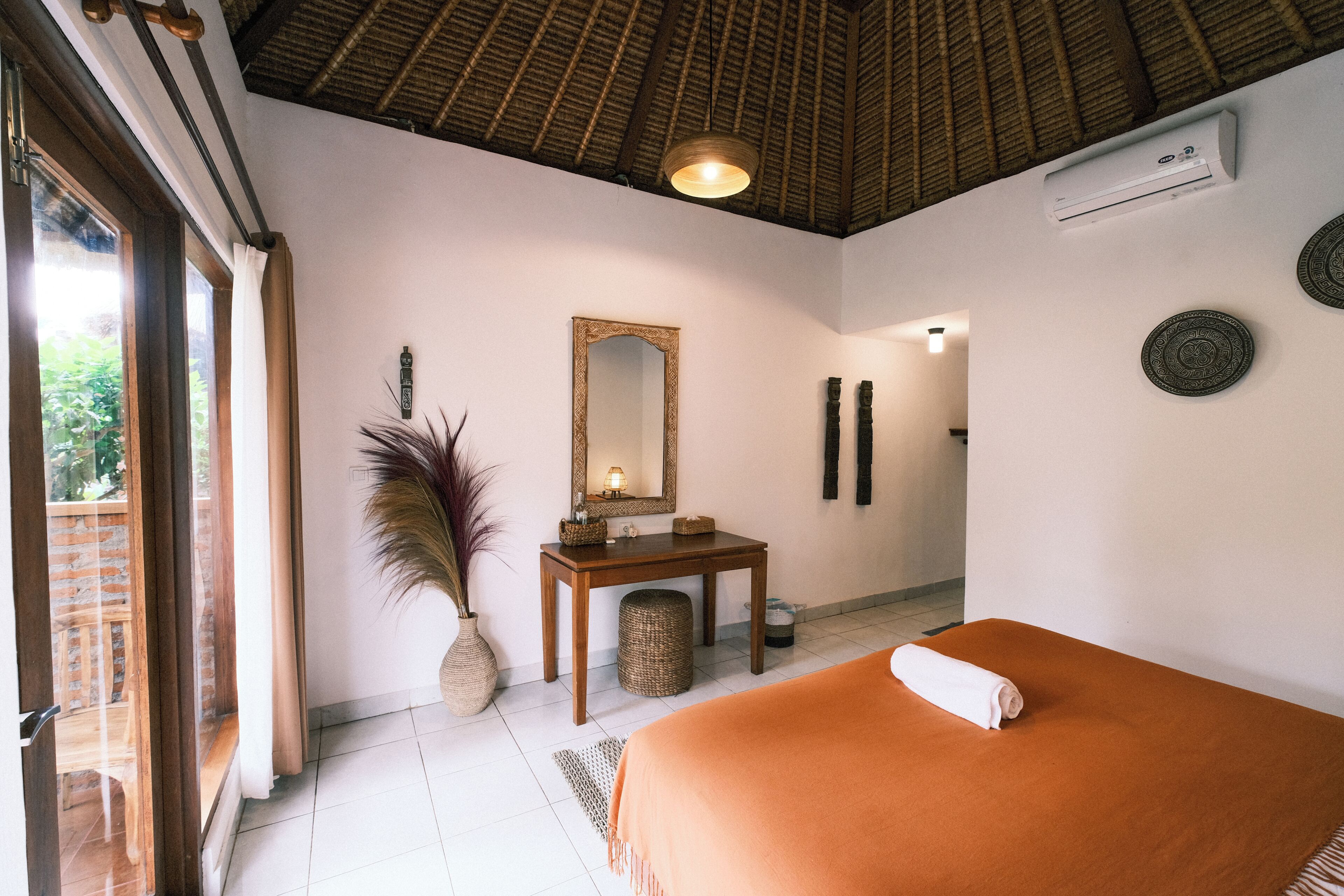 A bedroom with a bed, a vanity with a mirror, a small table, and a potted plant.