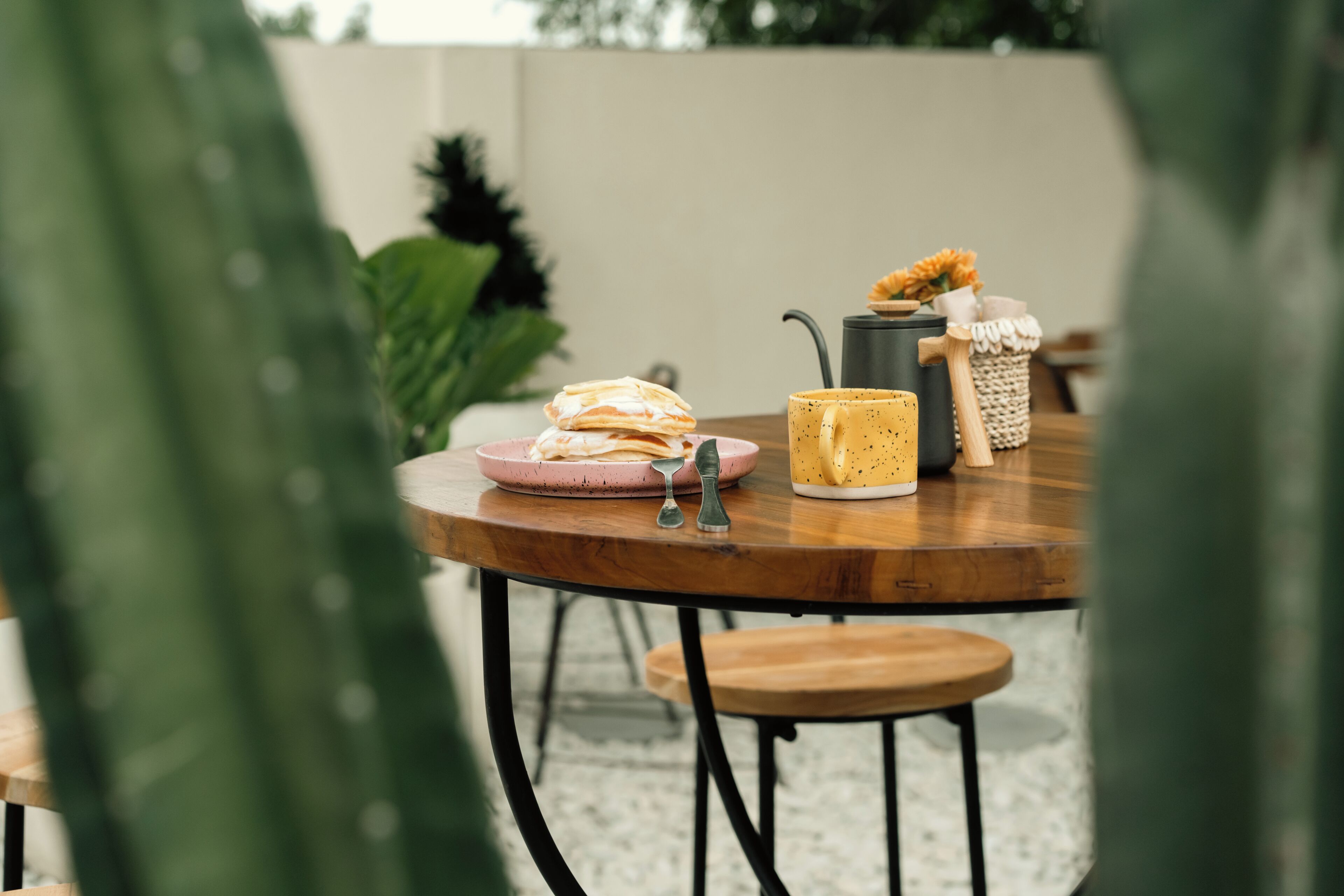 A round wooden table with a pink plate, a yellow mug, and a small basket with a plant.