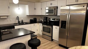 Una cocina moderna con armarios blancos, electrodomésticos de acero inoxidable, una encimera negra y dos taburetes negros.