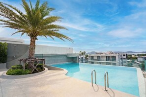A rooftop pool with a palm tree, a modern building, and a clear sky.