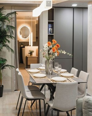 Ein moderner Essbereich mit einem Glastisch, grauen Stühlen und einer Blumenvase.