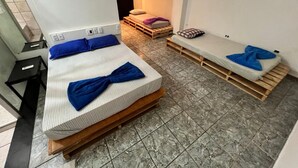 A compact room with two beds, each with a wooden frame and blue bedding. The room has a tiled floor and a small table with a chair. - Hostel Sideral (Campo Grande)