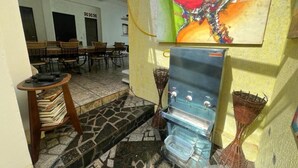 A room with a stone-tiled floor, a water dispenser, wicker baskets, and a bookshelf. - Hostel Sideral (Campo Grande)