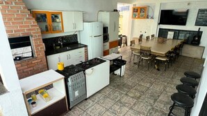 A compact kitchen with a gas stove, refrigerator, and a dining area with a table and chairs. - Hostel Sideral (Campo Grande)