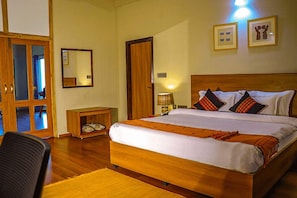 A hotel room with a wooden bed, a bedside table, a chair, and a mirror on the wall. - Foxtail Orchid (Bokakhat)