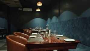 A restaurant with a long wooden table set for dining, blue cushioned seating, and hanging pendant lights. - Foxtail Orchid (Bokakhat)