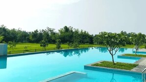 A swimming pool with clear blue water, surrounded by a grassy area and trees. - Foxtail Orchid (Bokakhat)
