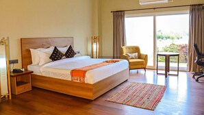 A hotel room with a large bed, a bedside table, a chair, a small table, and a view of the outdoors. - Foxtail Orchid (Bokakhat)
