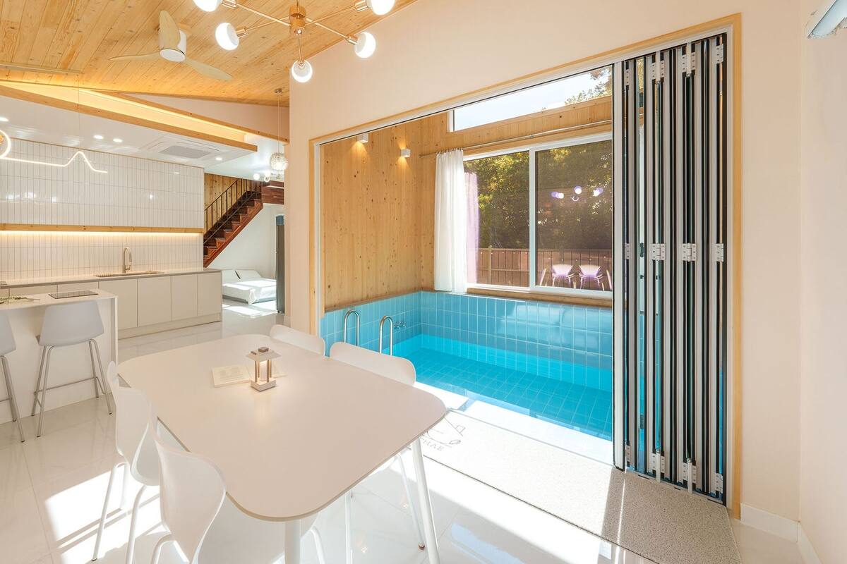 A modern kitchen with white cabinets, a dining area with a white table and chairs, and a large sliding glass door leading to a swimming pool area.