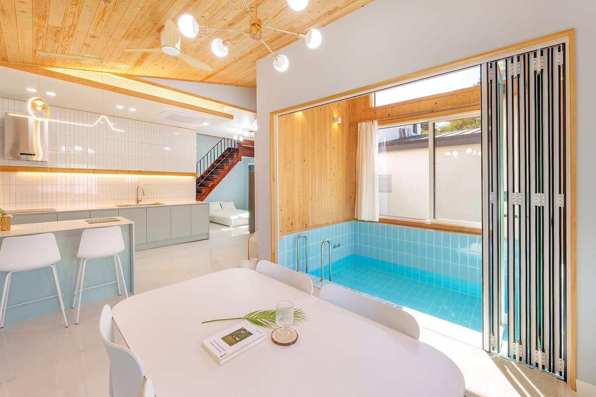A modern kitchen with white cabinets, a dining area with a white table, and a pool area with a blue pool.