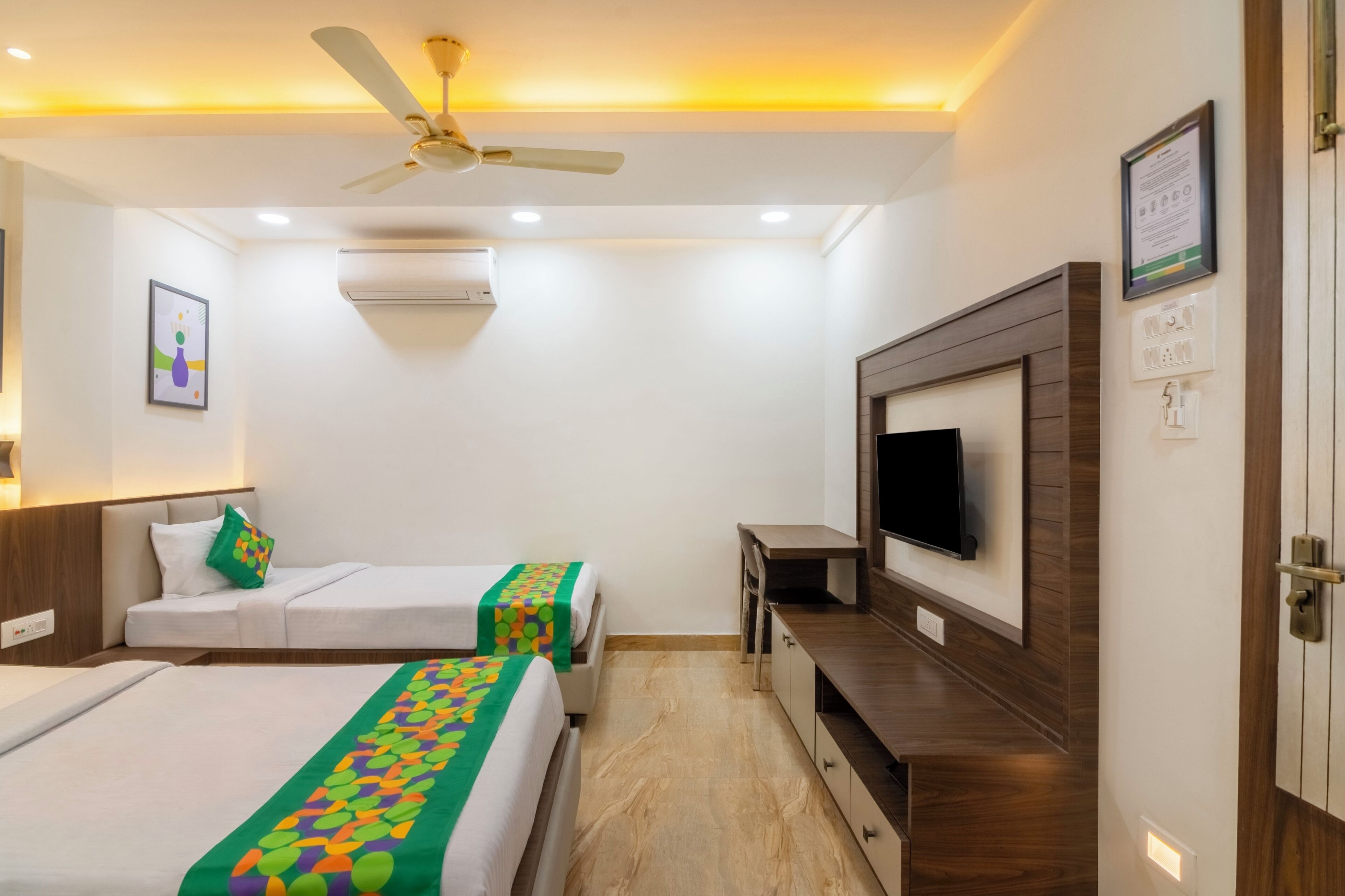 Habitación de hotel con dos camas, televisor, ventilador de techo y un armario de madera.