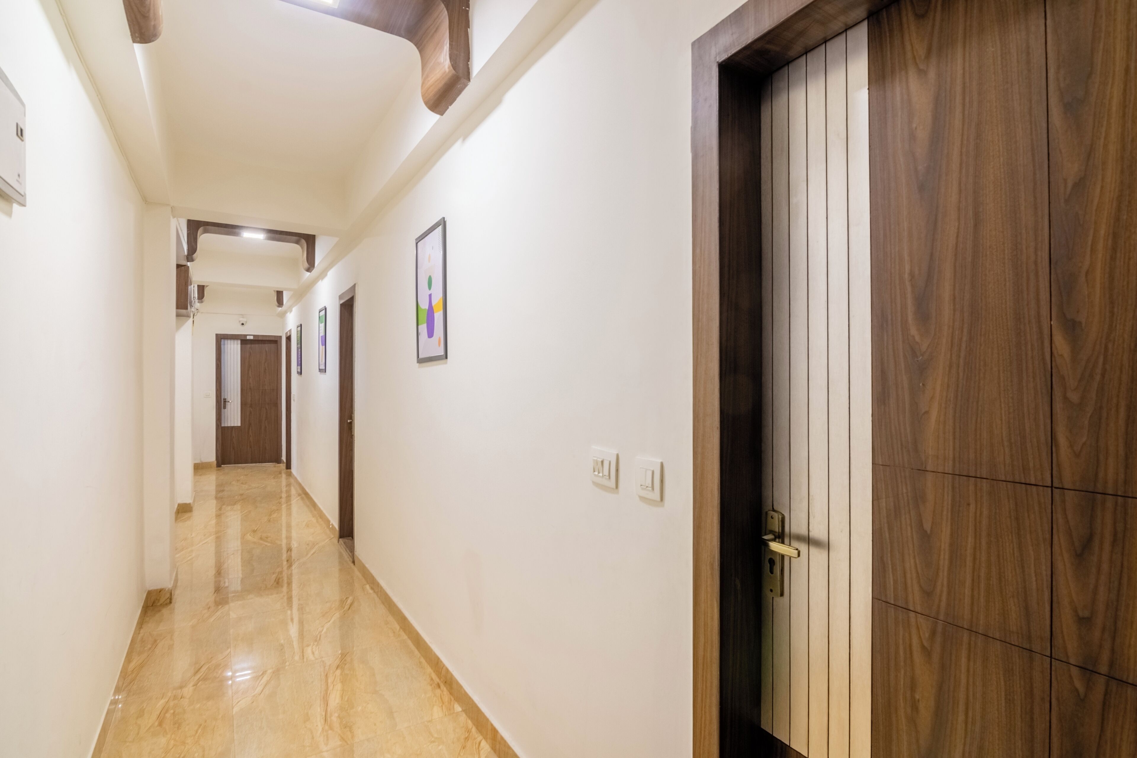 A hallway with a wooden door, white walls, and a marble floor.