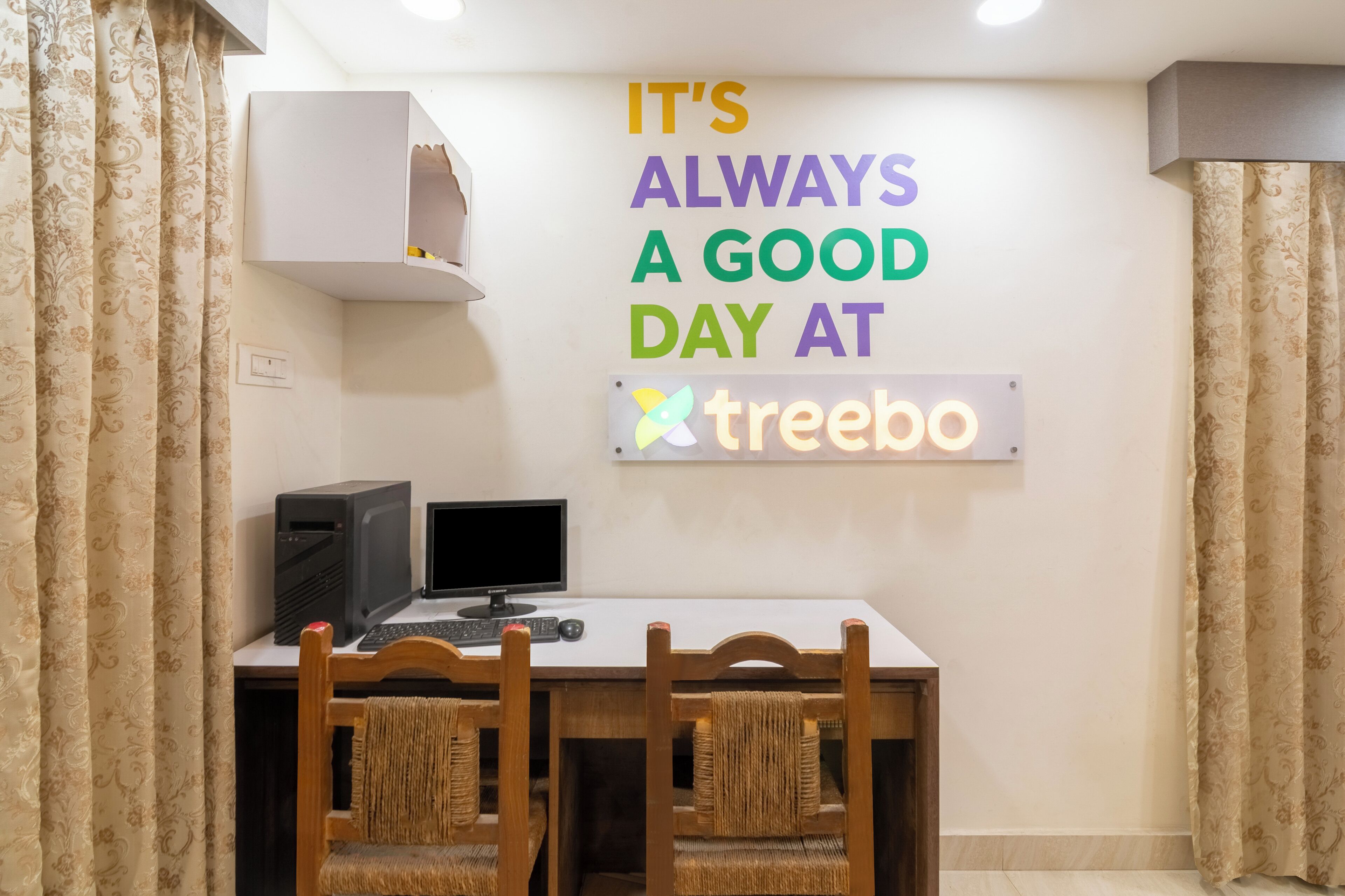 A room with a desk, two chairs, a computer, and a sign that reads "IT'S ALWAYS A GOOD DAY AT treebo".