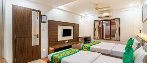A hotel room with two beds, a TV, a ceiling fan, and a window with curtains.