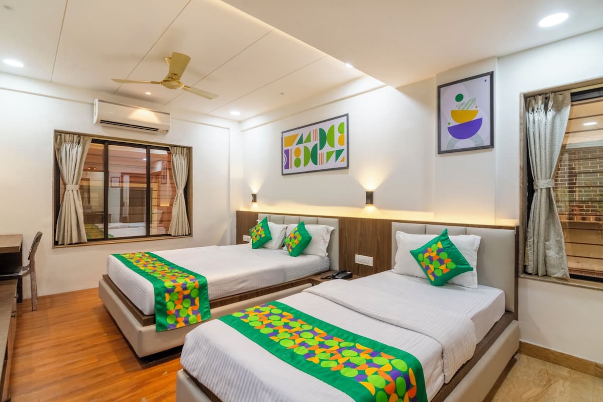 Quarto de hotel com duas camas, uma escrivaninha e uma cadeira. Há luminárias na parede, ar condicionado e ventilador de teto.