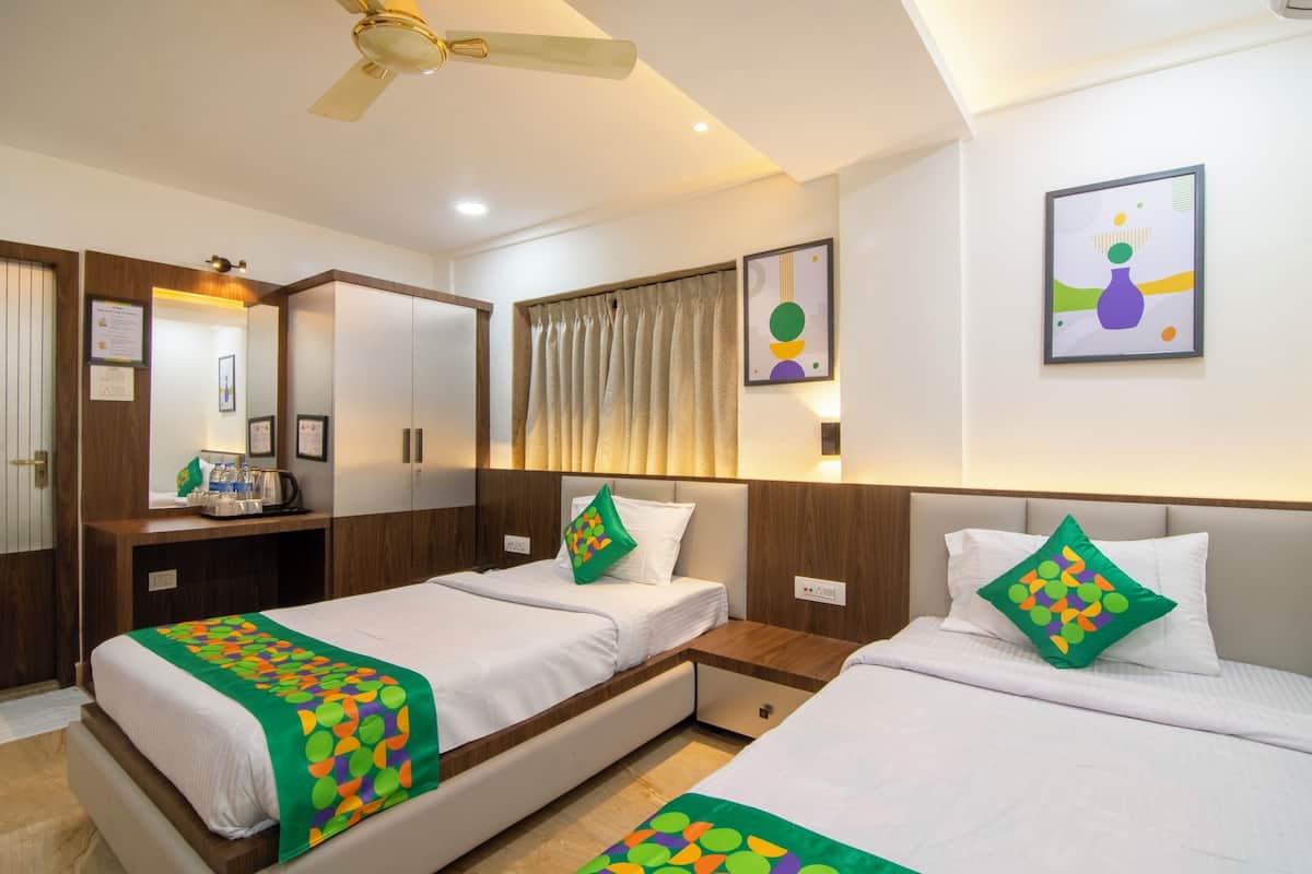 Quarto de hotel com duas camas de solteiro, uma escrivaninha com cadeira, um espelho e um ventilador de teto.