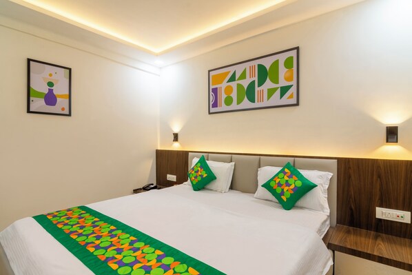 A hotel room with a large bed, two pillows with colorful patterns, a bedside table, and two wall-mounted lamps. - Treebo Petals Suites & Banquet - New Town (Barasat)