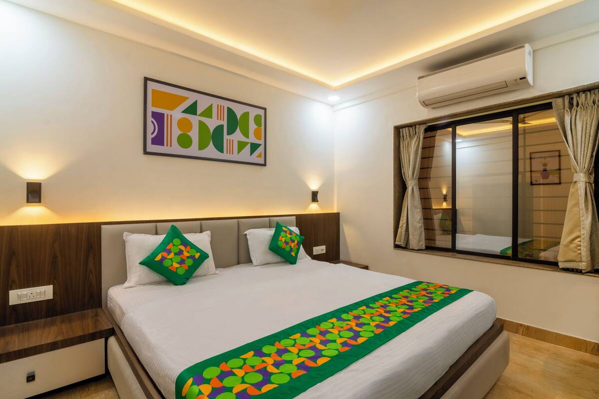 Quarto de hotel com cama, ar-condicionado fixado na parede e janela com cortinas.
