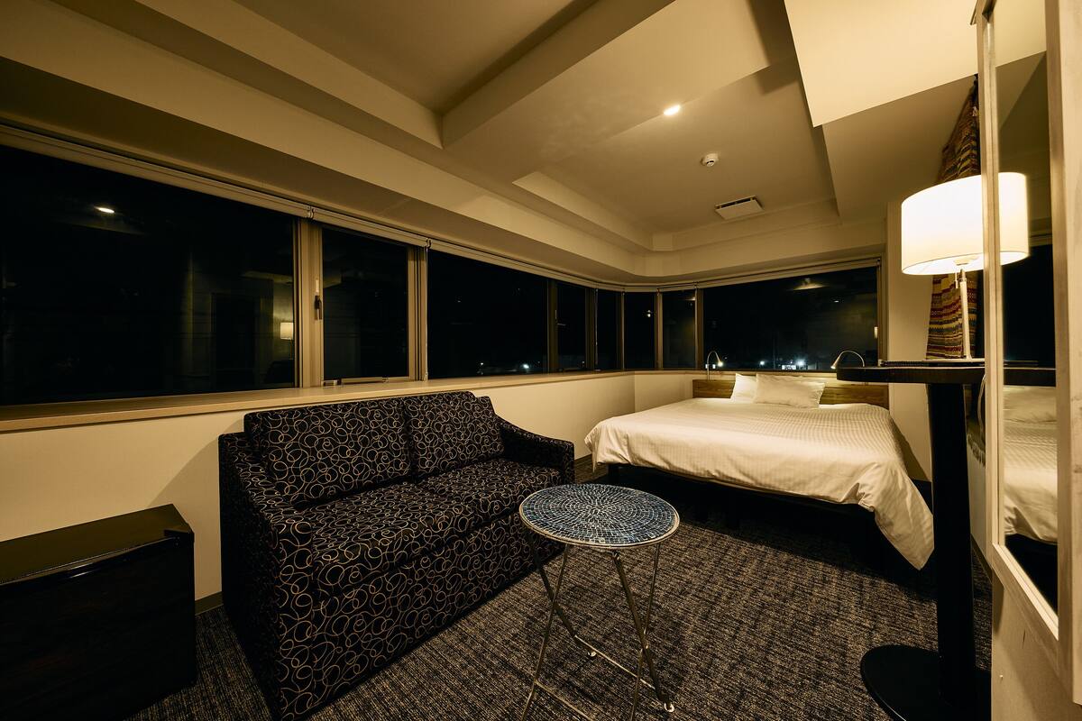 Ein Hotelzimmer mit einem Bett, einer Couch, einem kleinen runden Tisch und großen Fenstern.