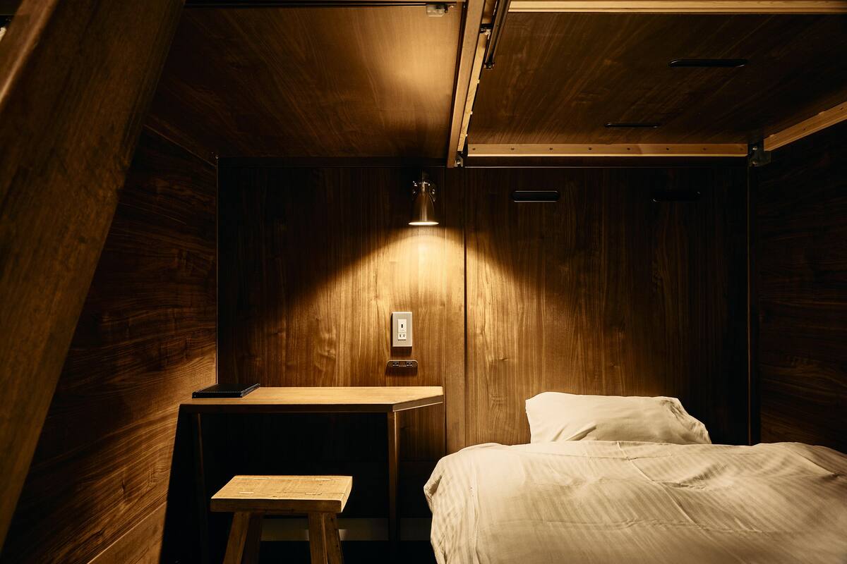 Ein Zimmer mit Holzboden, einem Bett, einem kleinen Tisch und einer Wandleuchte.